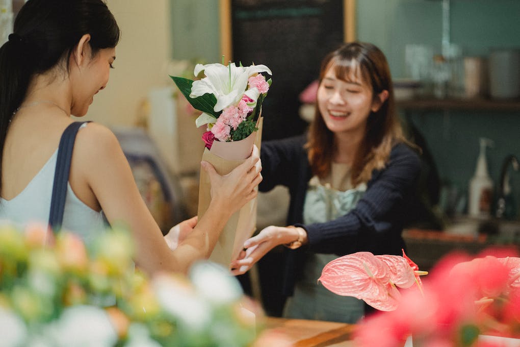 Happy Asian florist selling bouquet to female customer